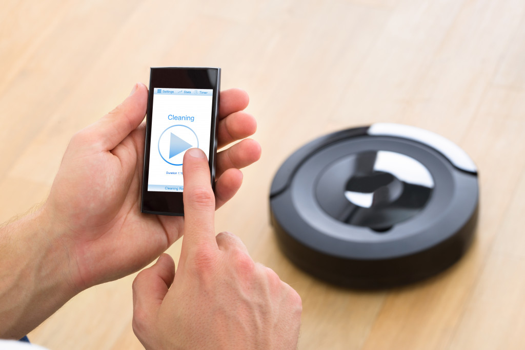 A person using a mobile device to set a robot vacuum cleaner to start cleaning