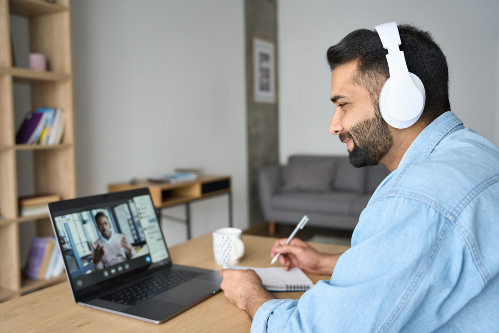 a businessman taking notes while watching a virtual training in the laptop