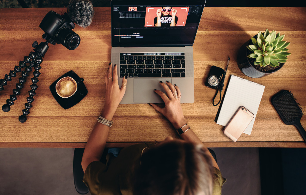 Young woman working on computer with cameras and accessories on table.