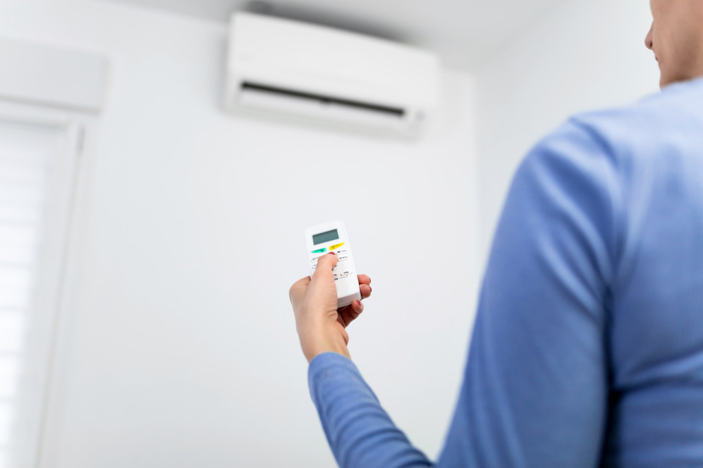 Woman holding a remote of a modern airconditioner unit at home.