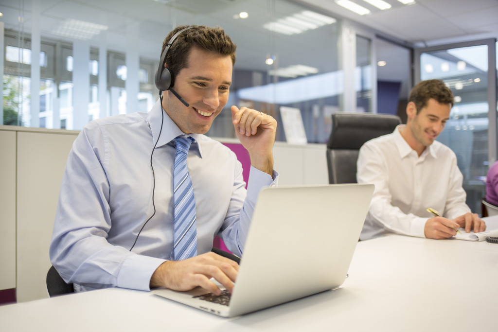 A businessman working with another man in an office while wearing headphones